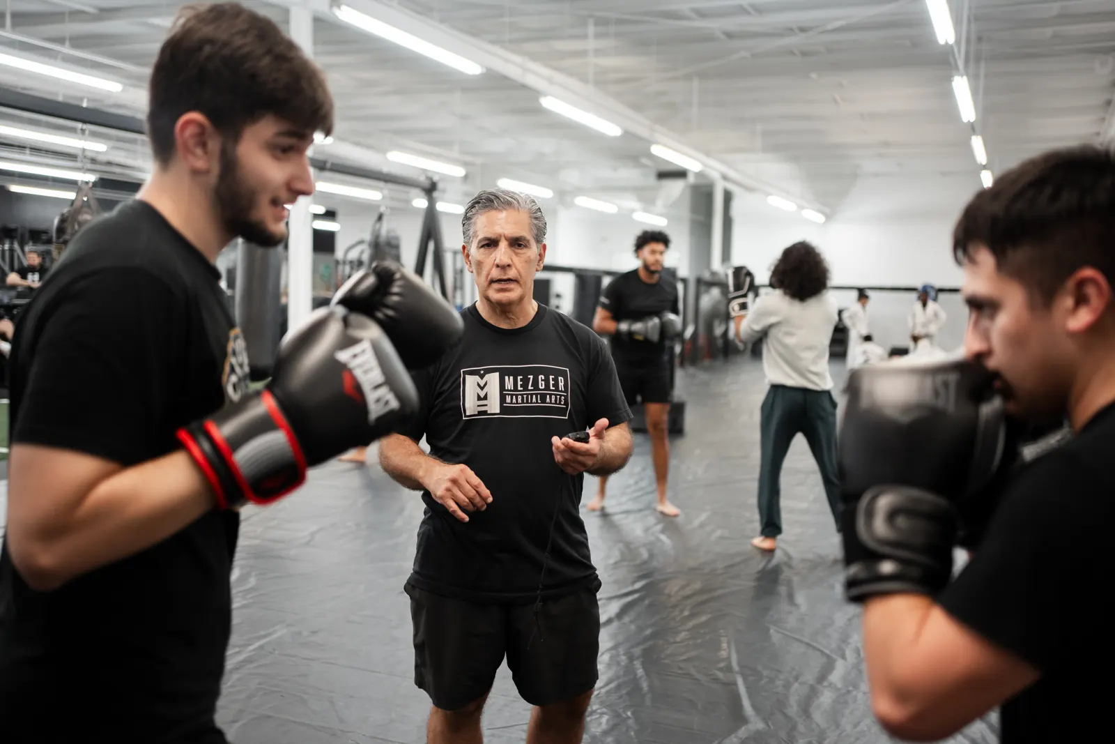 Coach working hands-on with two boxing students during a class at Mezger Martial Arts